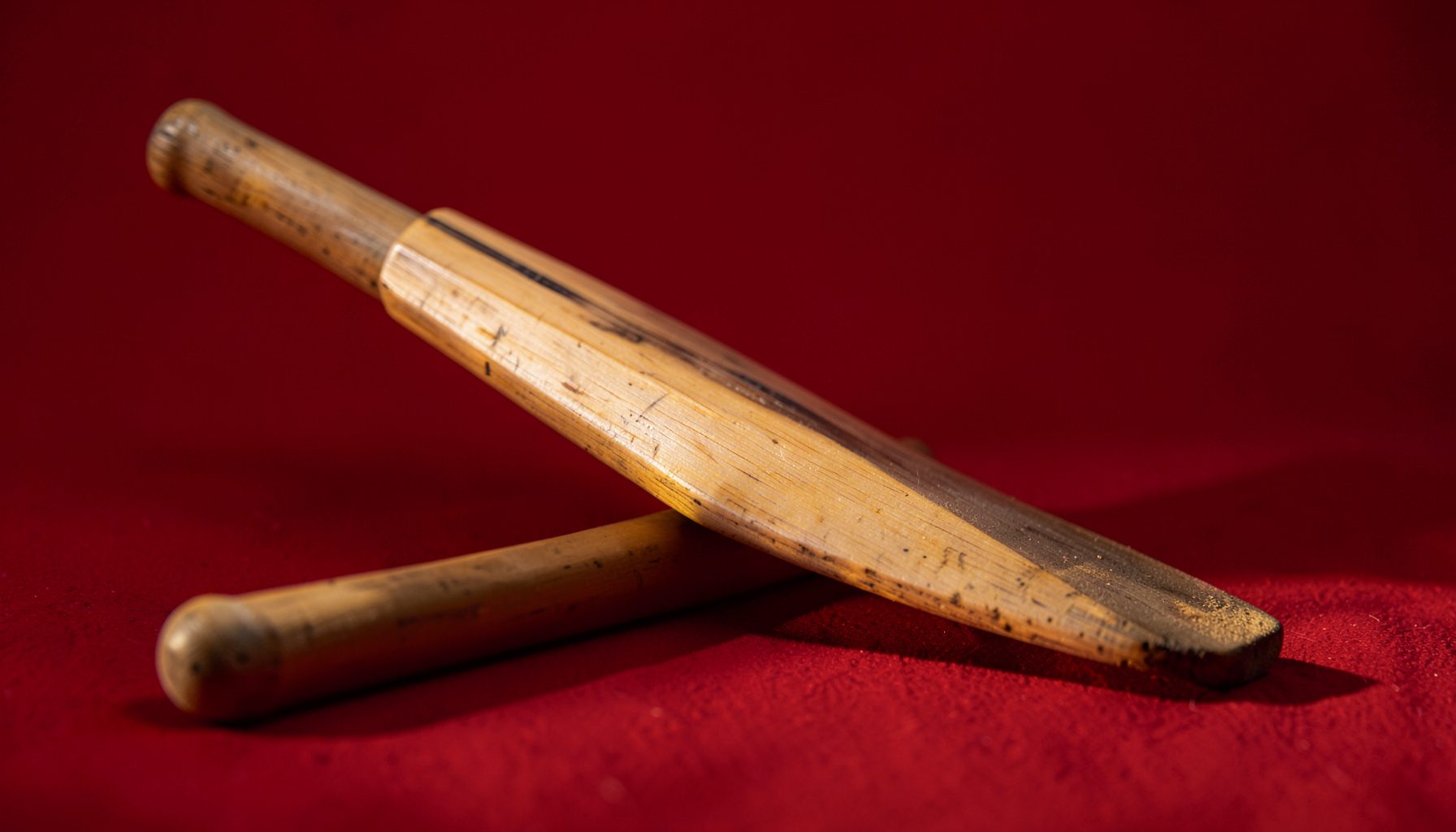 Close-up of a cricket bat resting on a pitch, warm sunlight casting long shadows, calm and focused mood