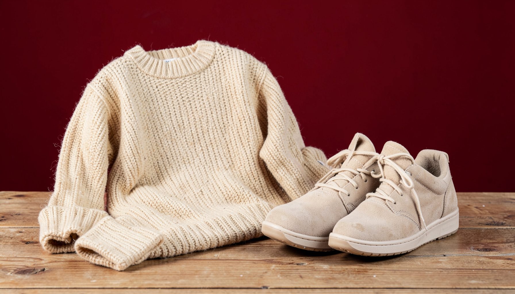Cozy knitwear and comfortable shoes arranged on a wooden surface, warm beige and cream tones, inviting and relaxed atmosphere