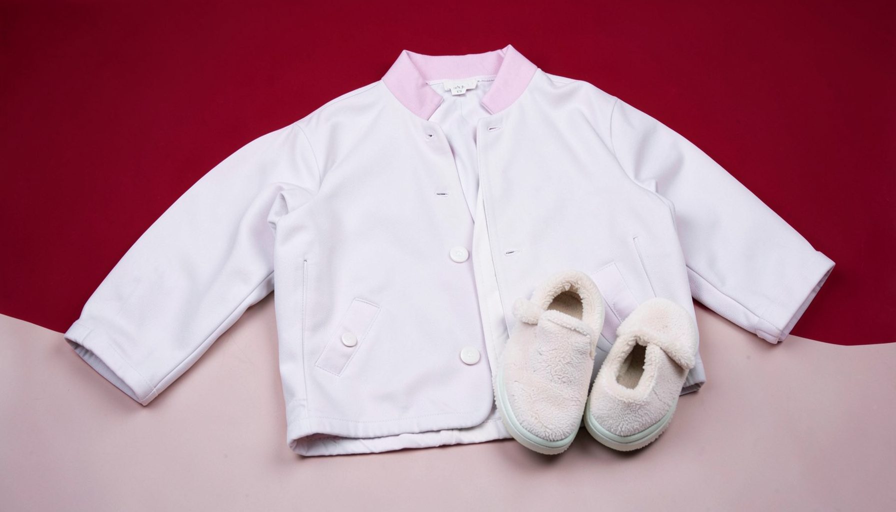 Soft pastel spring clothing laid flat on a light neutral surface, including a light jacket and cozy shoes, gentle and airy mood