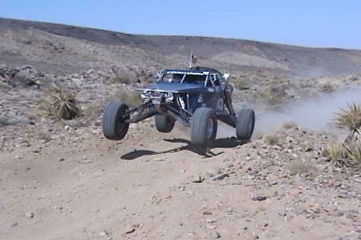 An off-road buggy vehicle catching air on a dirt trail in a desert landscape, dusty tan and blue tones, action mood